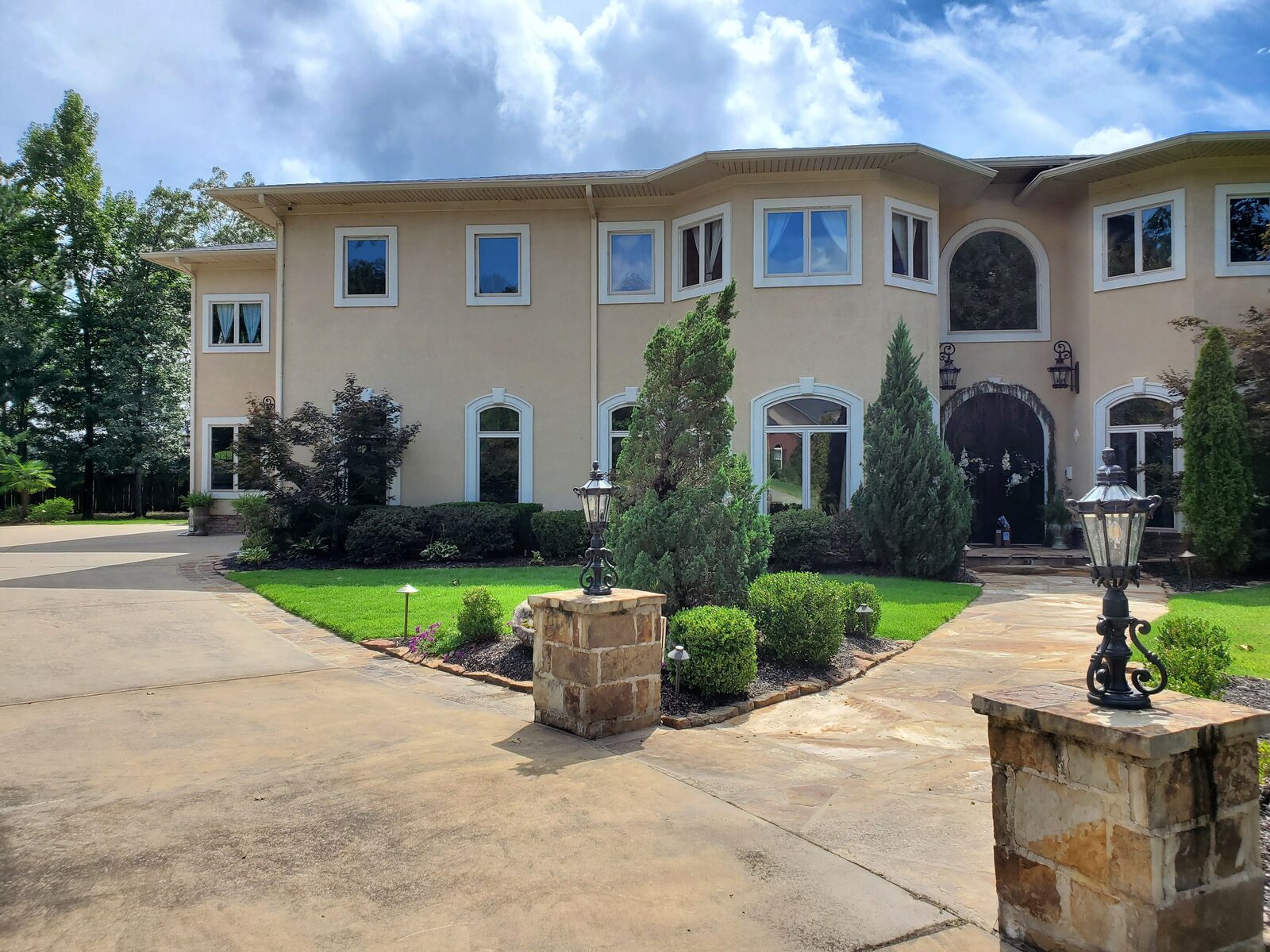 Brick estate front entrance with topiary cypresses, tight boxwood hedging, and stone columns